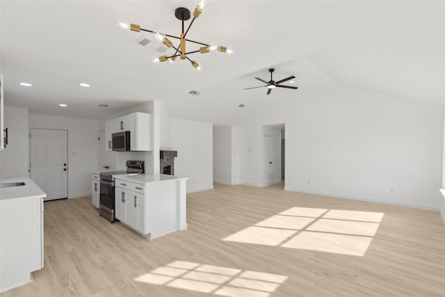 kitchen with vaulted ceiling, appliances with stainless steel finishes, decorative light fixtures, white cabinets, and light hardwood / wood-style floors