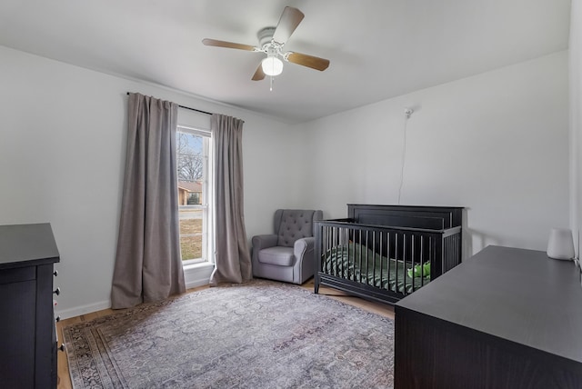 bedroom with wood-type flooring, a crib, multiple windows, and ceiling fan