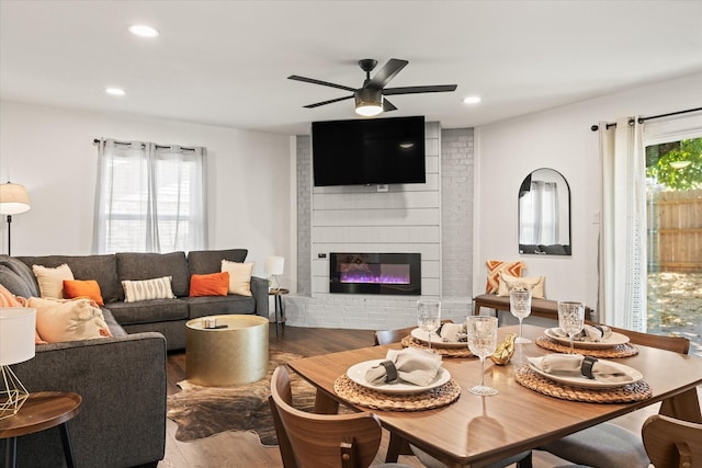 living area with a ceiling fan, a brick fireplace, recessed lighting, and wood finished floors