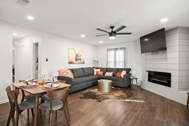 living room featuring ceiling fan, a large fireplace, and dark hardwood / wood-style floors