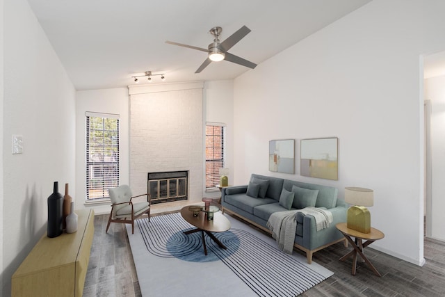 living room with wood-type flooring, vaulted ceiling, ceiling fan, and a large fireplace