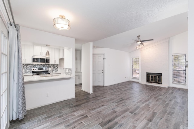 kitchen with backsplash, white cabinets, a fireplace, lofted ceiling, and stainless steel appliances