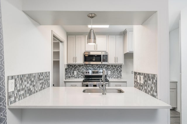 kitchen featuring kitchen peninsula, decorative light fixtures, sink, tasteful backsplash, and stainless steel appliances