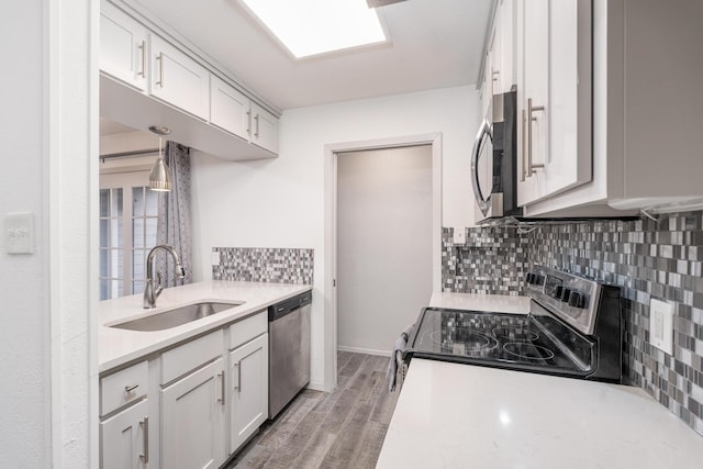 kitchen featuring appliances with stainless steel finishes, sink, decorative light fixtures, white cabinets, and hardwood / wood-style floors