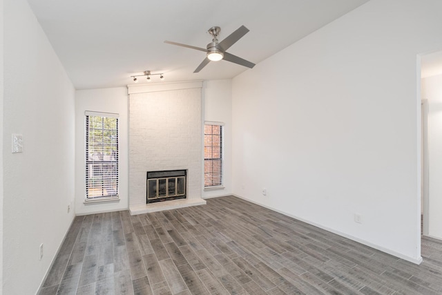 unfurnished living room featuring a fireplace, hardwood / wood-style flooring, track lighting, ceiling fan, and lofted ceiling