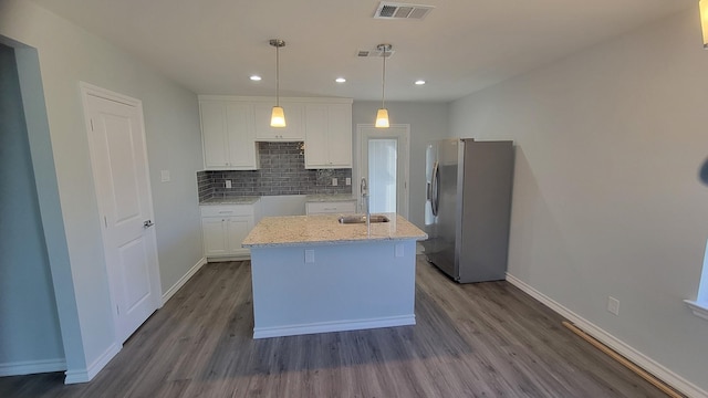 kitchen featuring pendant lighting, stainless steel refrigerator with ice dispenser, white cabinetry, an island with sink, and sink