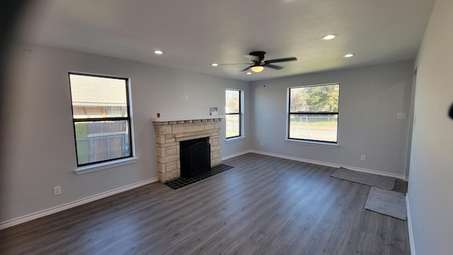 unfurnished living room featuring dark hardwood / wood-style flooring, a stone fireplace, and ceiling fan