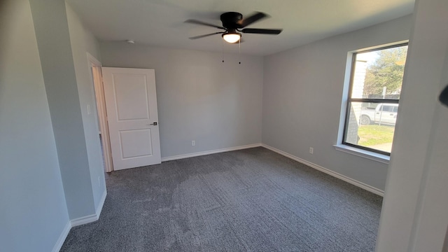 empty room featuring dark colored carpet, ceiling fan, and a wealth of natural light