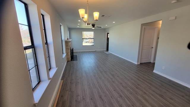 spare room with dark hardwood / wood-style floors, a stone fireplace, and a notable chandelier