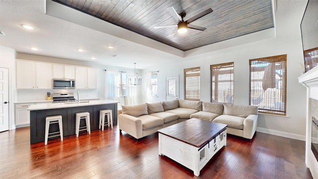 living room featuring a raised ceiling, sink, wood ceiling, ceiling fan with notable chandelier, and dark hardwood / wood-style floors