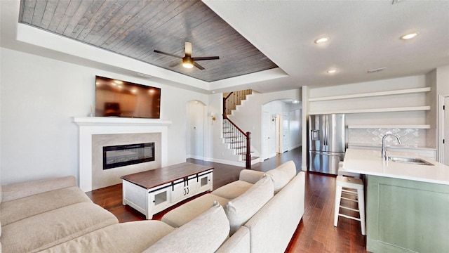 living room with wood ceiling, dark wood-type flooring, sink, a raised ceiling, and ceiling fan