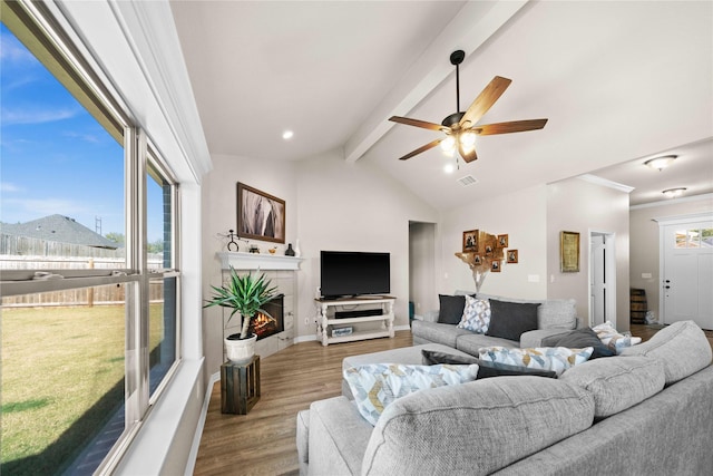 living room featuring ceiling fan, vaulted ceiling with beams, light hardwood / wood-style floors, and a tiled fireplace