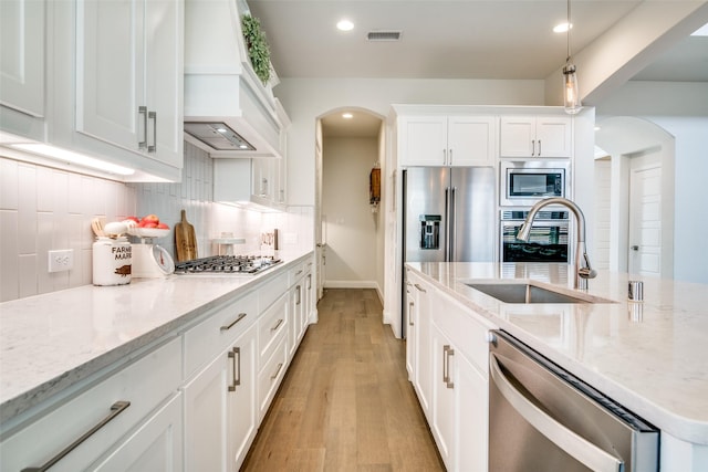 kitchen with sink, custom exhaust hood, white cabinetry, light stone countertops, and stainless steel appliances