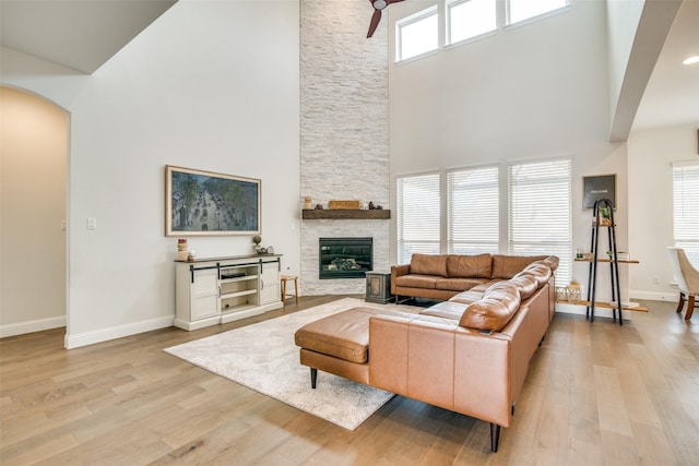 living room featuring a high ceiling, a stone fireplace, and light wood-type flooring