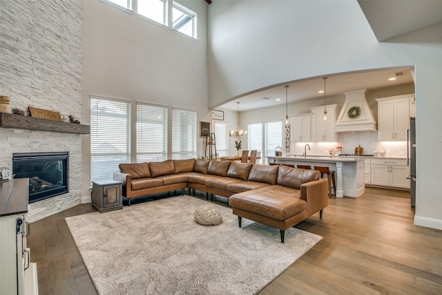 living room with sink, light wood-type flooring, a towering ceiling, and an inviting chandelier