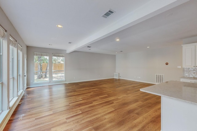 unfurnished living room with light hardwood / wood-style floors and beam ceiling