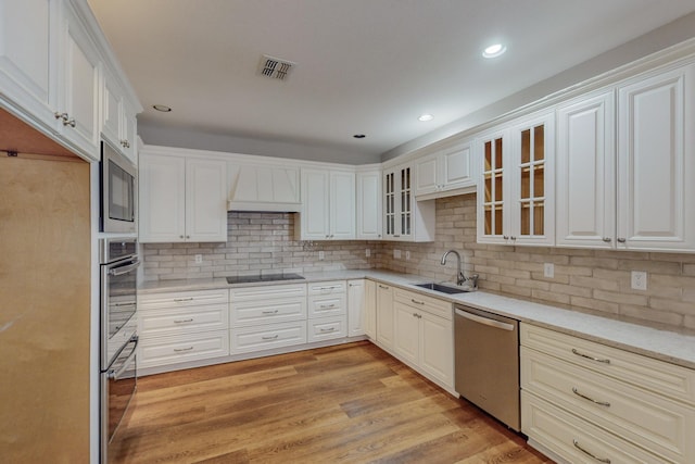 kitchen with custom range hood, decorative backsplash, sink, light hardwood / wood-style flooring, and stainless steel appliances