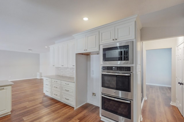 kitchen with backsplash, white cabinetry, light hardwood / wood-style flooring, and stainless steel appliances