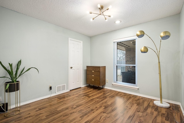 unfurnished bedroom featuring an inviting chandelier, dark hardwood / wood-style floors, and a textured ceiling