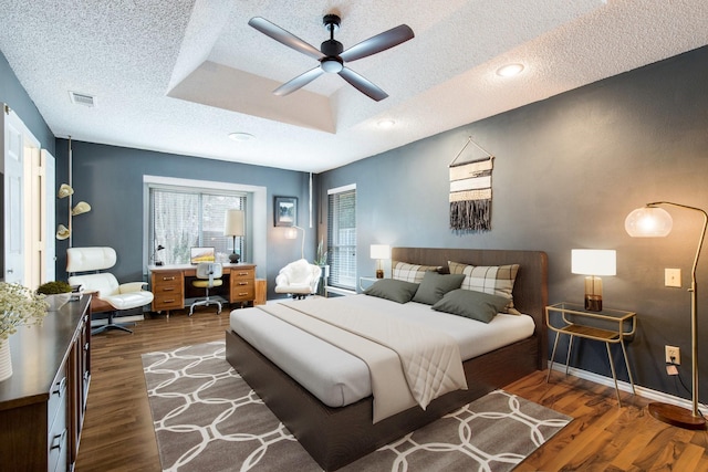 bedroom with ceiling fan, a tray ceiling, dark hardwood / wood-style floors, and a textured ceiling