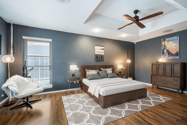 bedroom with wood-type flooring, a raised ceiling, and a textured ceiling