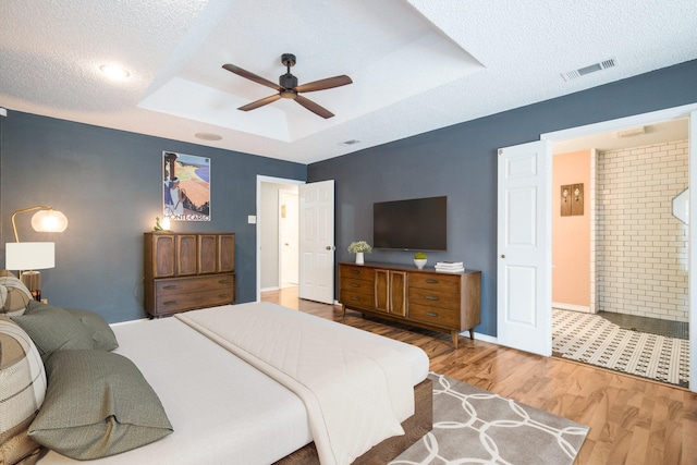 bedroom featuring ensuite bathroom, a textured ceiling, a tray ceiling, hardwood / wood-style flooring, and ceiling fan