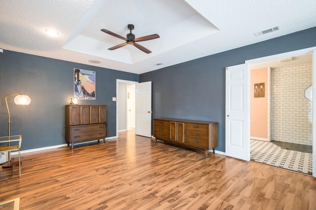 bedroom featuring ceiling fan, a tray ceiling, wood-type flooring, and a textured ceiling