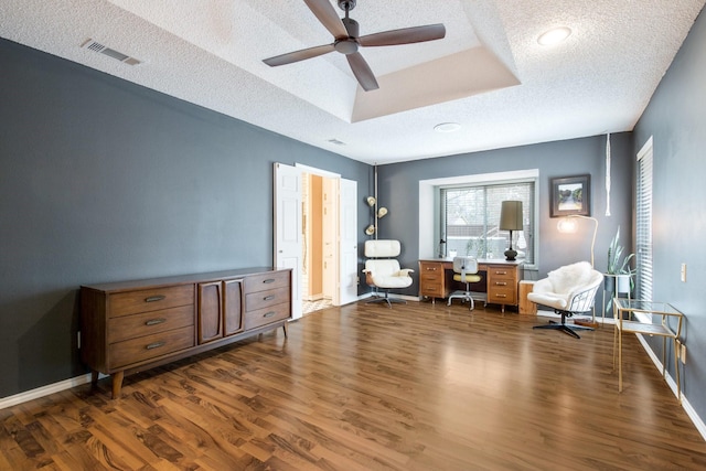 living area with ceiling fan, dark hardwood / wood-style floors, a textured ceiling, and a tray ceiling