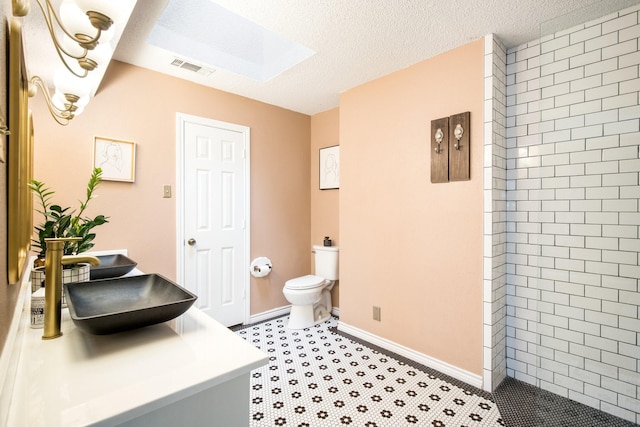 bathroom featuring sink, a skylight, tiled shower, a textured ceiling, and toilet