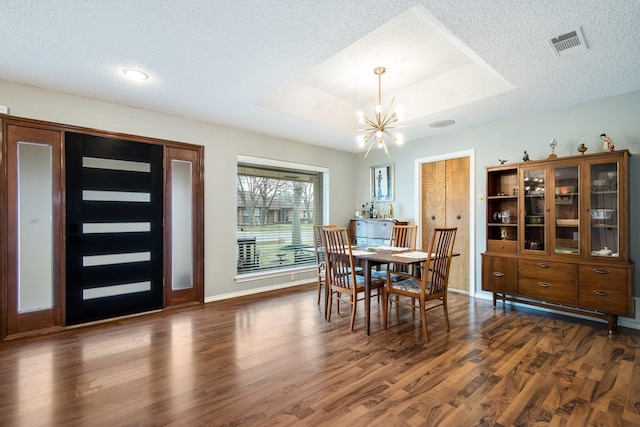 dining room with a tray ceiling, dark wood-type flooring, a textured ceiling, and a chandelier