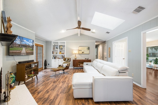 living room with vaulted ceiling with skylight, ceiling fan, crown molding, dark wood-type flooring, and built in shelves