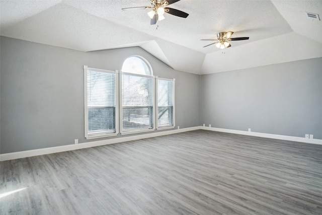 unfurnished room featuring ceiling fan, a raised ceiling, hardwood / wood-style floors, a textured ceiling, and lofted ceiling