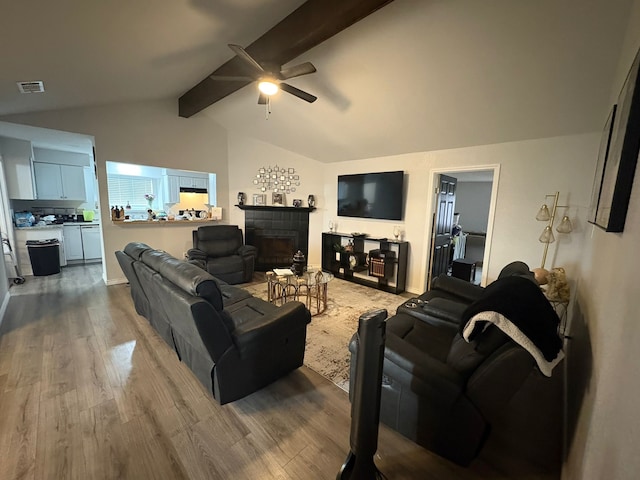 living room with ceiling fan, hardwood / wood-style floors, a tile fireplace, and lofted ceiling with beams