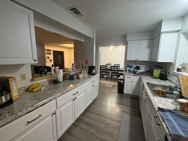 kitchen with light stone countertops, sink, white cabinetry, and dark wood-type flooring