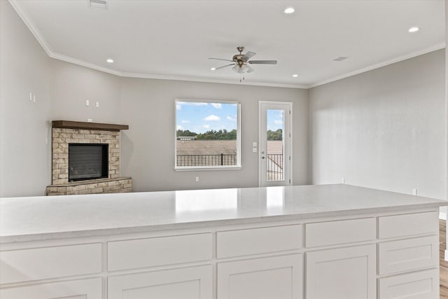 interior space with a fireplace, white cabinets, ceiling fan, light hardwood / wood-style floors, and crown molding