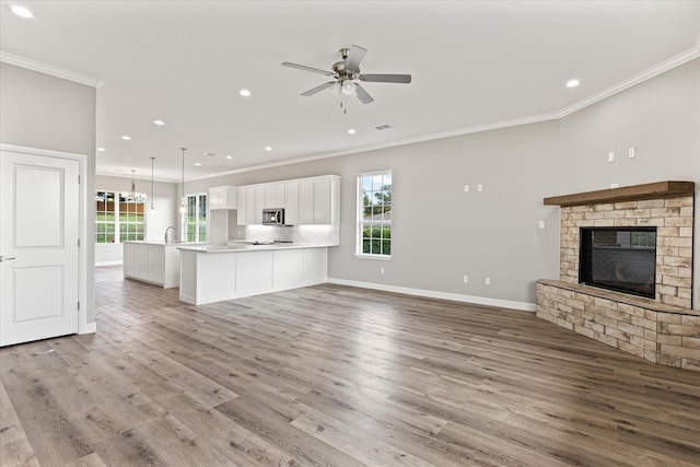 unfurnished living room with ceiling fan with notable chandelier, a fireplace, ornamental molding, and light wood-type flooring