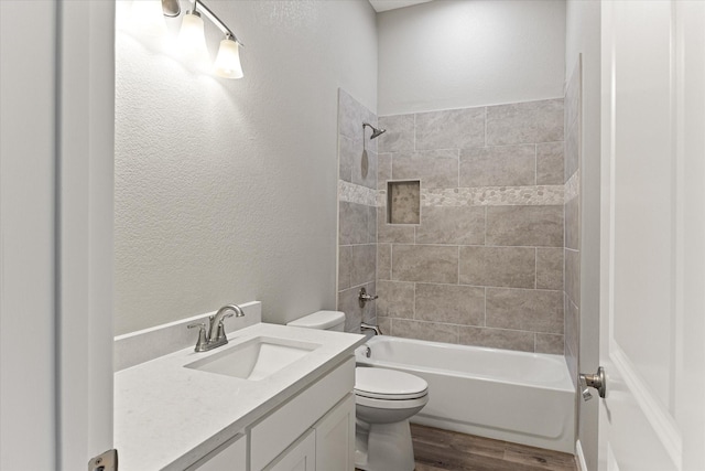 full bathroom with tiled shower / bath combo, vanity, hardwood / wood-style floors, and toilet