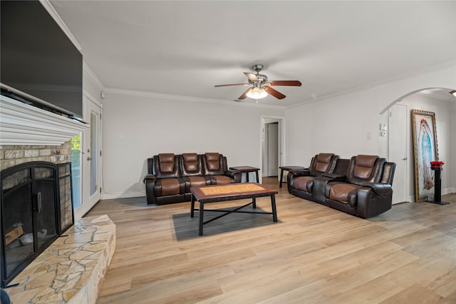 living room with a fireplace, ornamental molding, ceiling fan, and light wood-type flooring