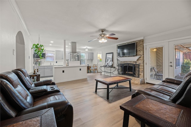 living room featuring a brick fireplace, crown molding, light hardwood / wood-style floors, and ceiling fan