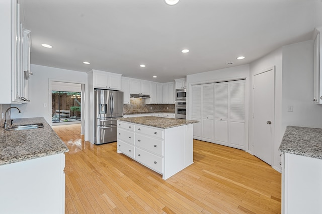 kitchen featuring light stone countertops, a center island, white cabinetry, stainless steel appliances, and sink