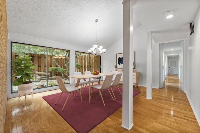 dining space featuring a textured ceiling, lofted ceiling, an inviting chandelier, and light wood-type flooring