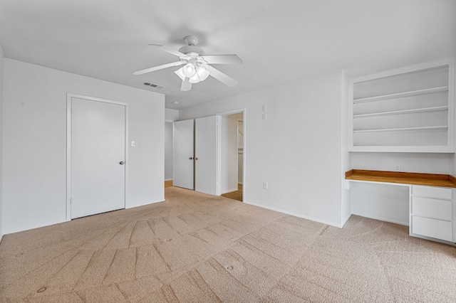 unfurnished bedroom with built in desk, ceiling fan, and light carpet