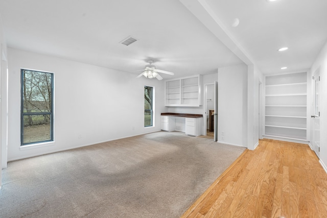 unfurnished living room featuring light carpet, built in features, plenty of natural light, and ceiling fan