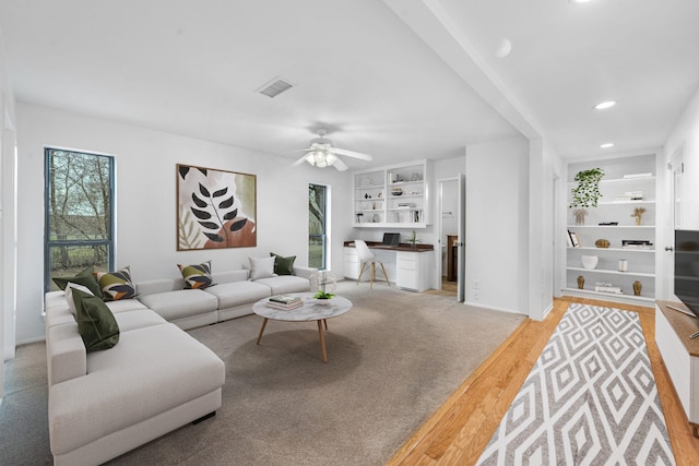 living room with built in features, light wood-type flooring, and ceiling fan