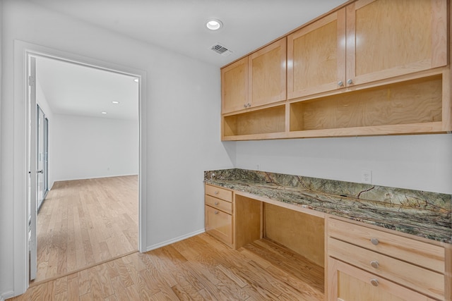 kitchen with built in desk, dark stone counters, light brown cabinetry, and light hardwood / wood-style floors