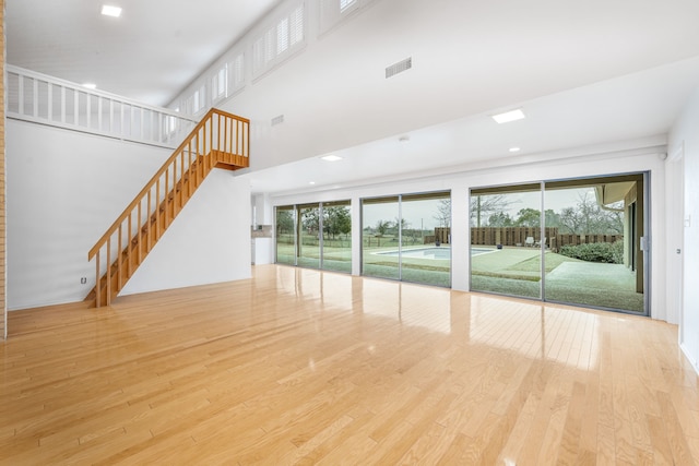 unfurnished living room with light hardwood / wood-style floors, a towering ceiling, and a wealth of natural light