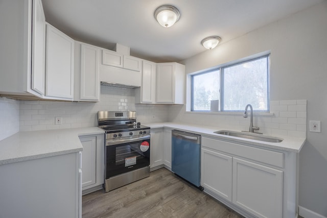 kitchen with appliances with stainless steel finishes, sink, white cabinets, tasteful backsplash, and light wood-type flooring