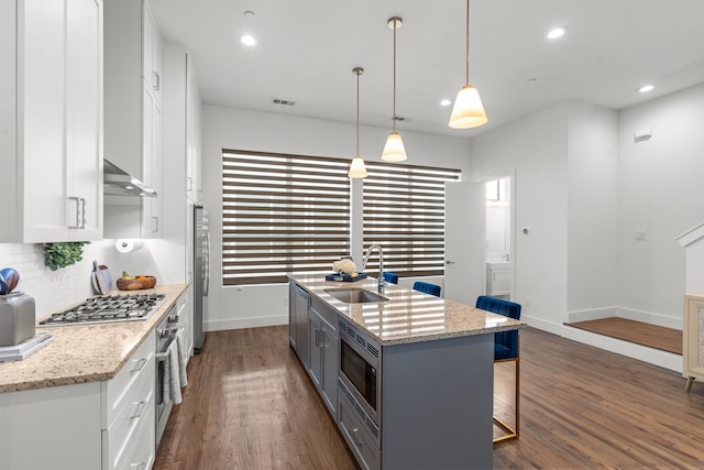 kitchen with white cabinets, decorative light fixtures, stainless steel appliances, sink, and a center island with sink