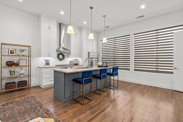 kitchen with a kitchen island with sink, wall chimney range hood, white cabinets, light stone counters, and dark hardwood / wood-style floors