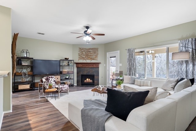 living room with ceiling fan, a healthy amount of sunlight, a tile fireplace, and wood-type flooring